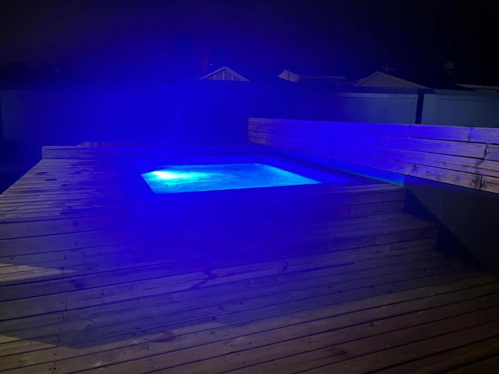 Illuminated swimming pool at night with blue LED lighting and wooden deck