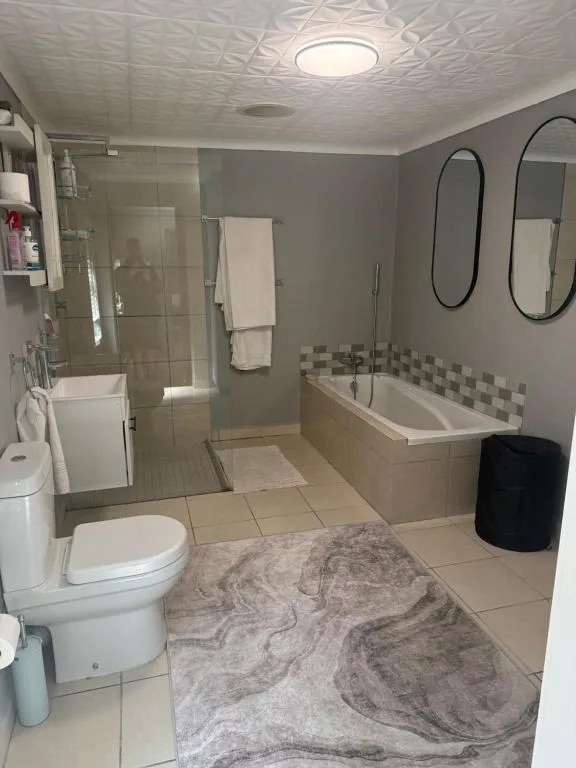 Spacious bathroom with walk-in shower, bathtub, toilet, and dual mirrors