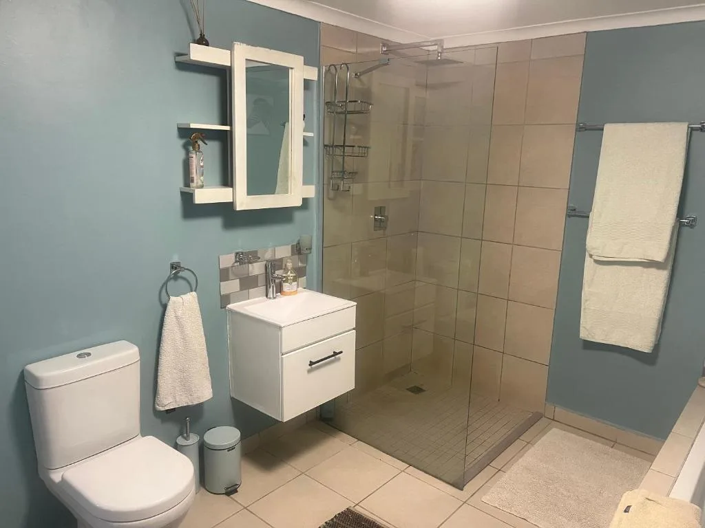 Modern bathroom with walk-in shower, white vanity, toilet, and lit mirror cabinet