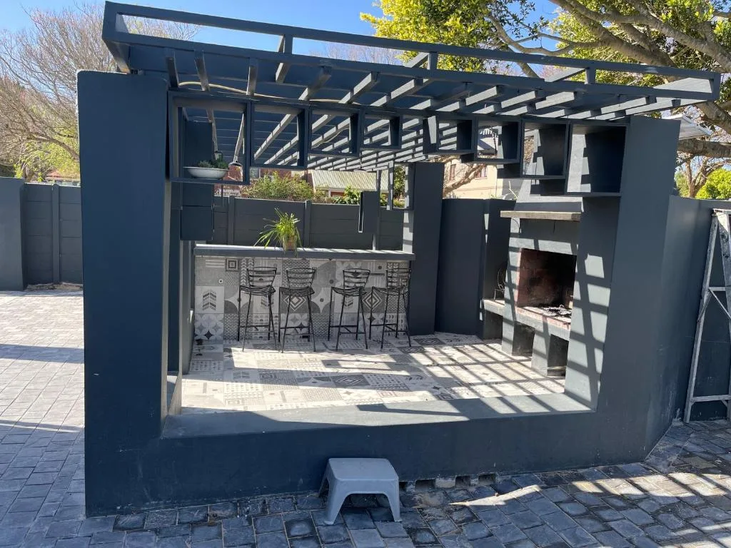Modern outdoor braai area with pergola, bar seating, and fireplace
