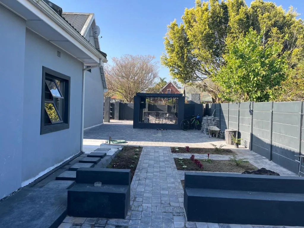 Modern white cottage with paved courtyard, black gate, and manicured gardens