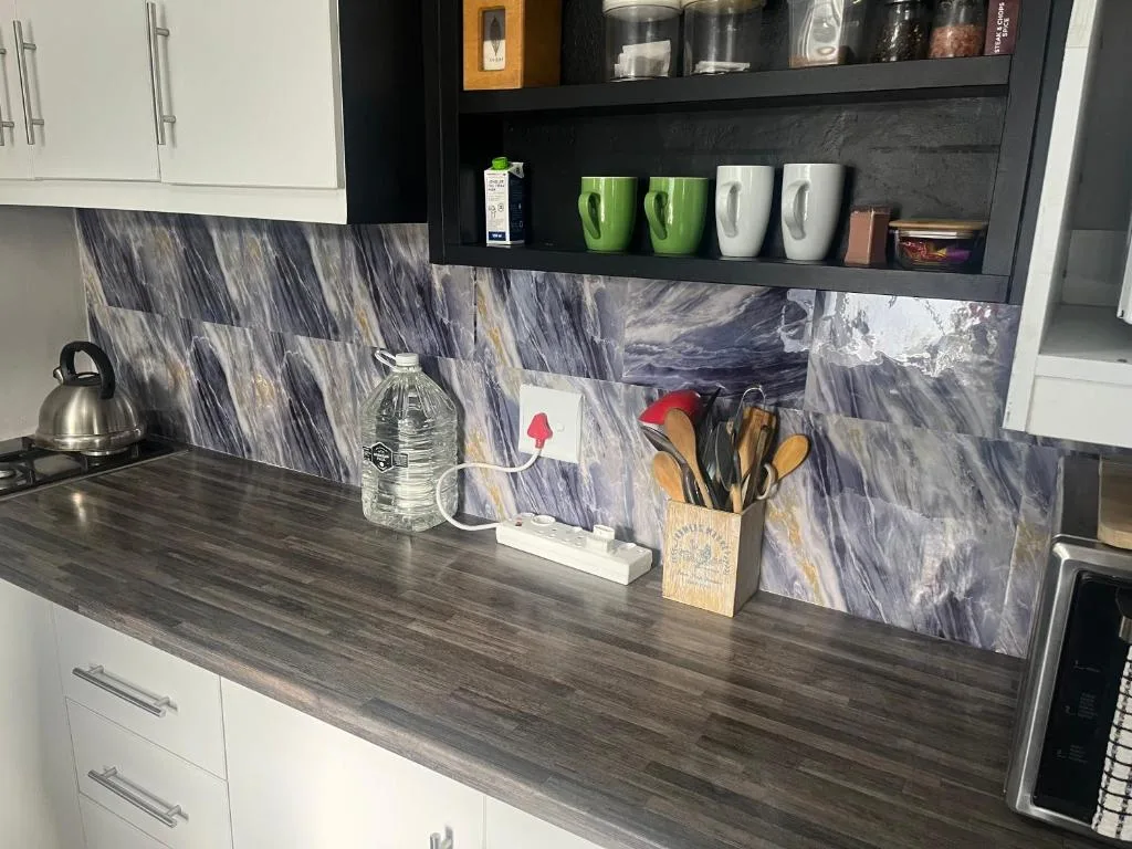Modern kitchen counter with marble backsplash, white cabinetry, and black shelving