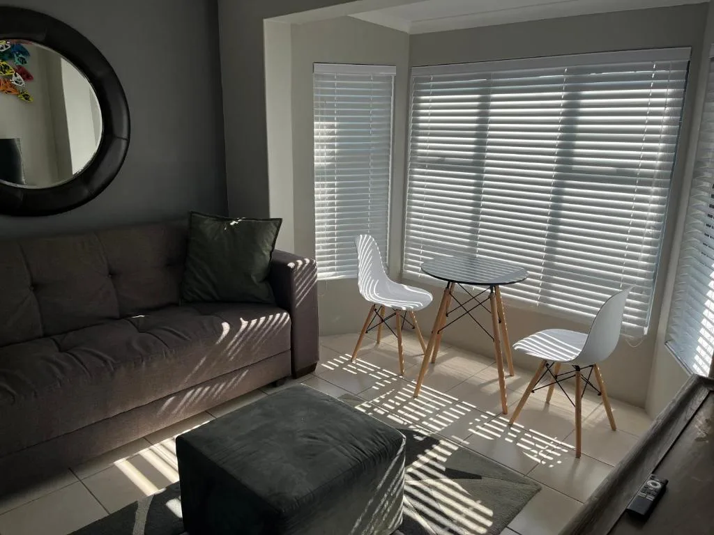 Modern lounge with black sofa, white chairs, and bright shuttered windows