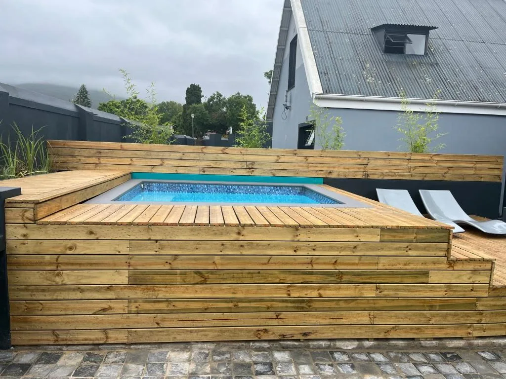 Modern sunken pool with wooden deck and lounge chairs beside house