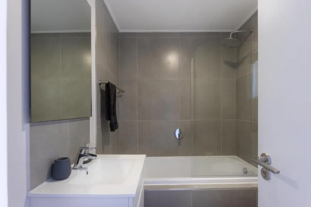 Modern bathroom with tiled shower enclosure, white vanity sink, and bathtub