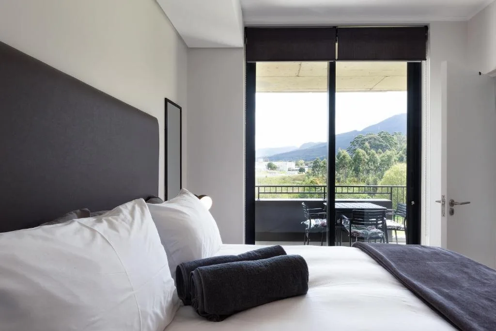 Modern bedroom with black headboard, white pillows, mountain and valley views through glass doors