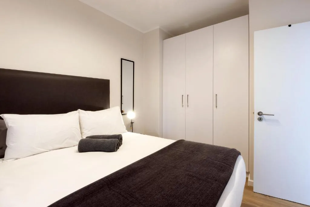 Modern bedroom with queen bed, dark headboard, white pillows, built-in wardrobe