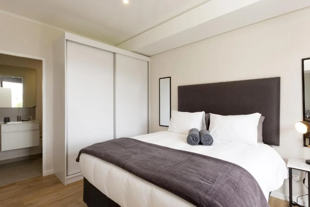 Modern bedroom with queen bed, dark headboard, and ensuite bathroom access