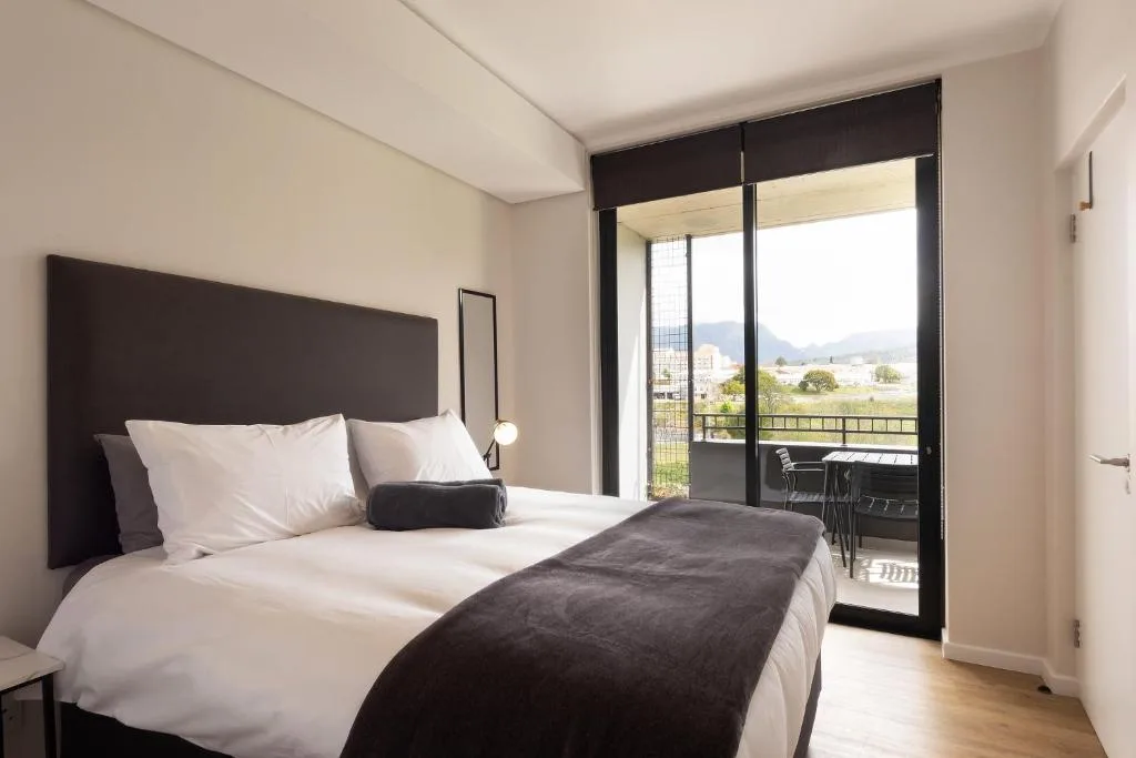 Modern bedroom with dark headboard, white bedding, and scenic mountain views through glass doors
