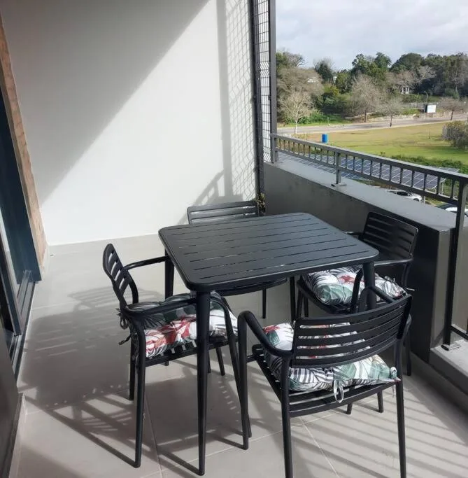 Outdoor balcony with black dining table and chairs overlooking green gardens