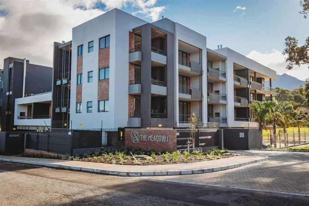 Modern multi-story apartment building with brick and white facade, entrance signage visible
