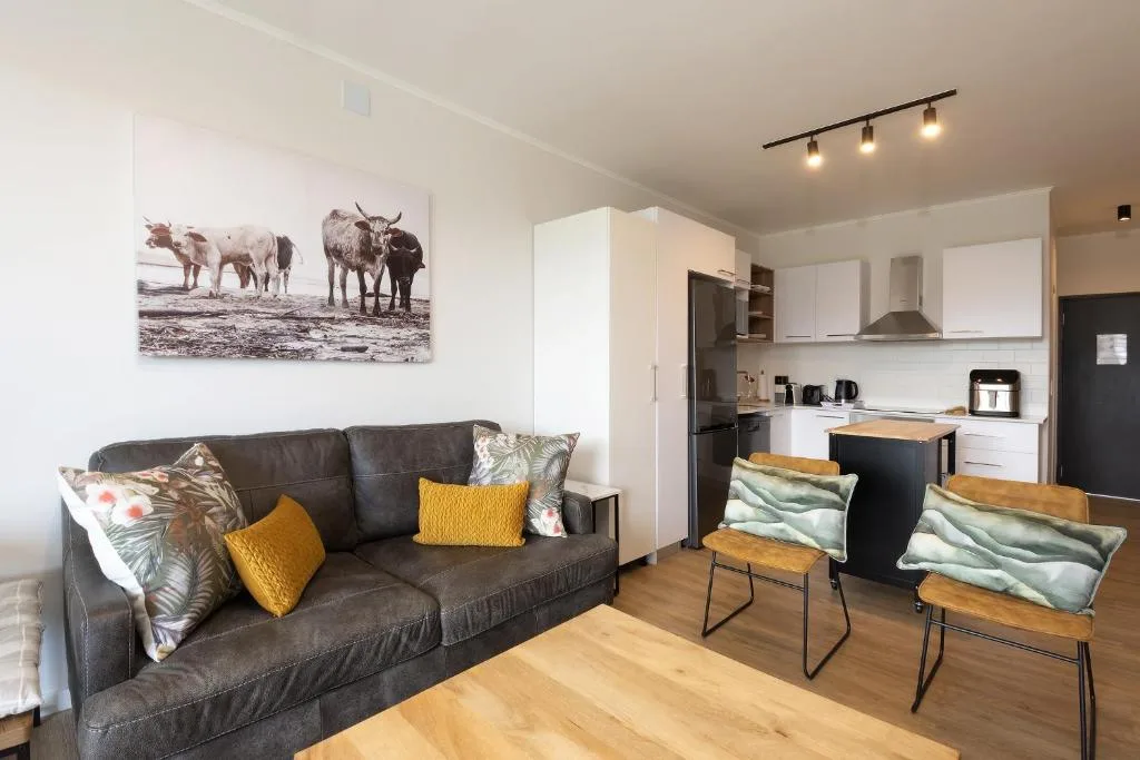 Modern lounge with dark leather sofa, colorful cushions, and open kitchen view