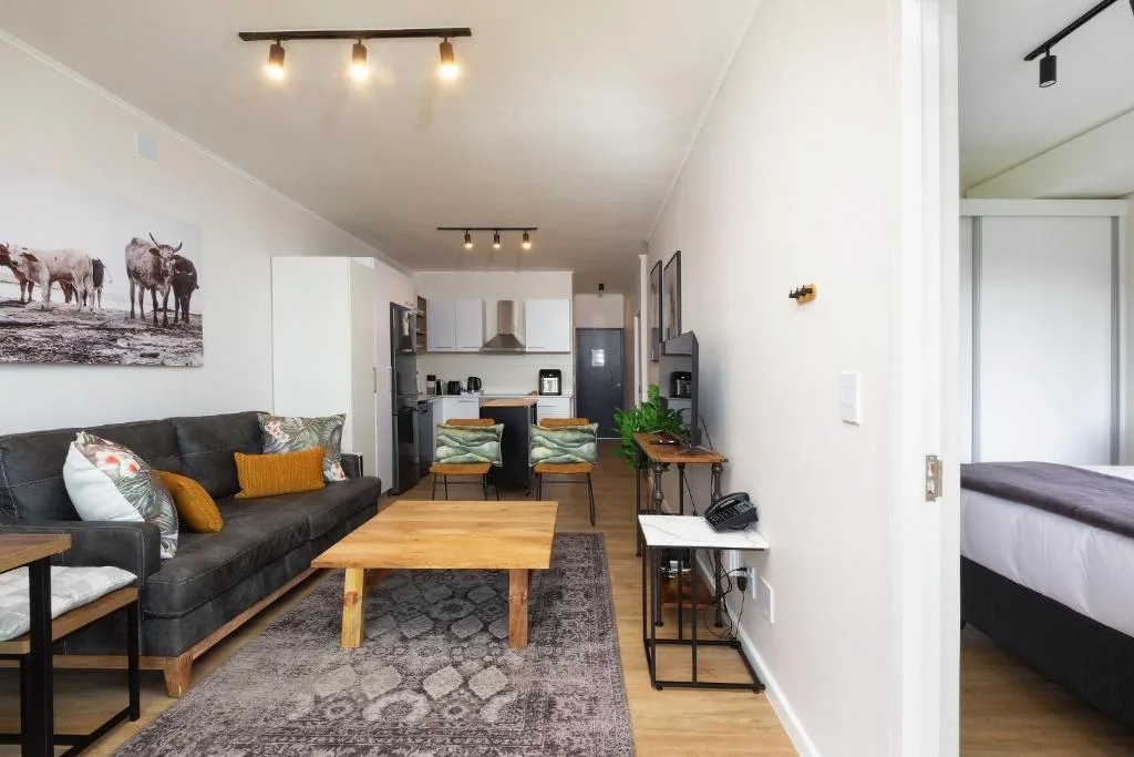 Open-plan lounge with black sofa, wooden coffee table, and kitchen visible beyond