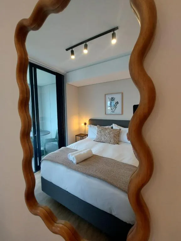 Modern bedroom with queen bed, wooden-framed mirror, and ensuite bathroom door