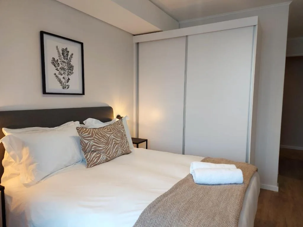 Modern bedroom with queen bed, white linens, zebra-print pillow, and botanical wall art