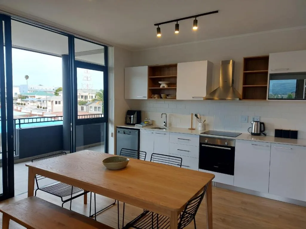 Modern kitchen with white cabinetry, dining table, and ocean views through glass doors