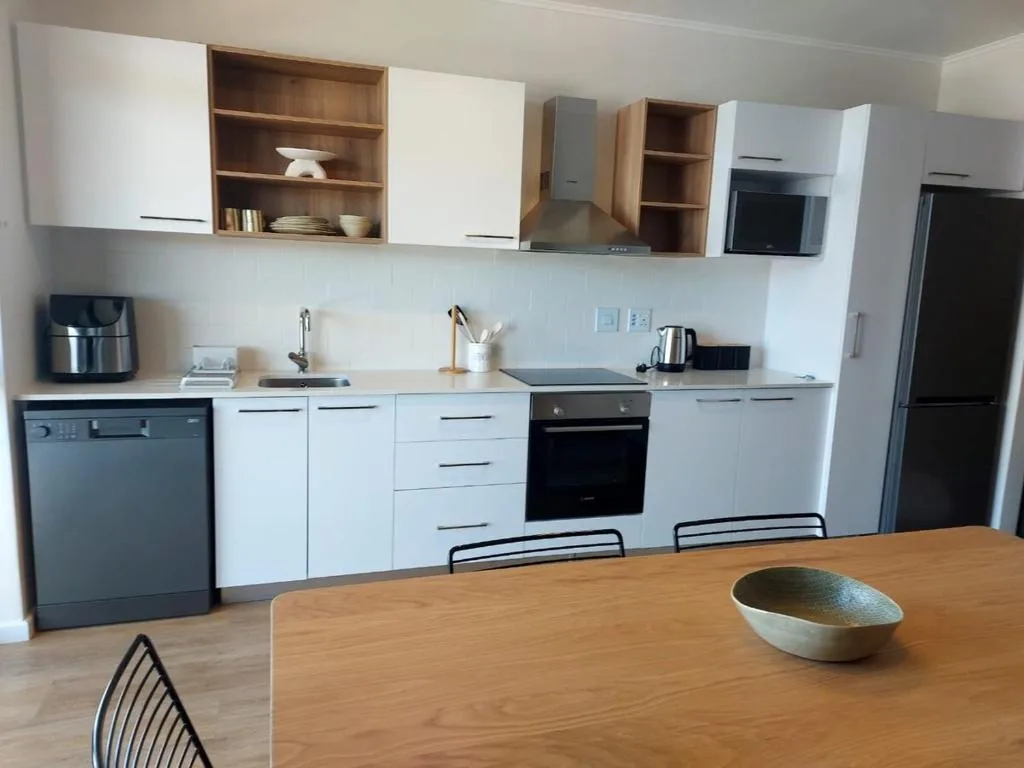 Modern kitchen with white cabinetry, black appliances, and wooden dining table