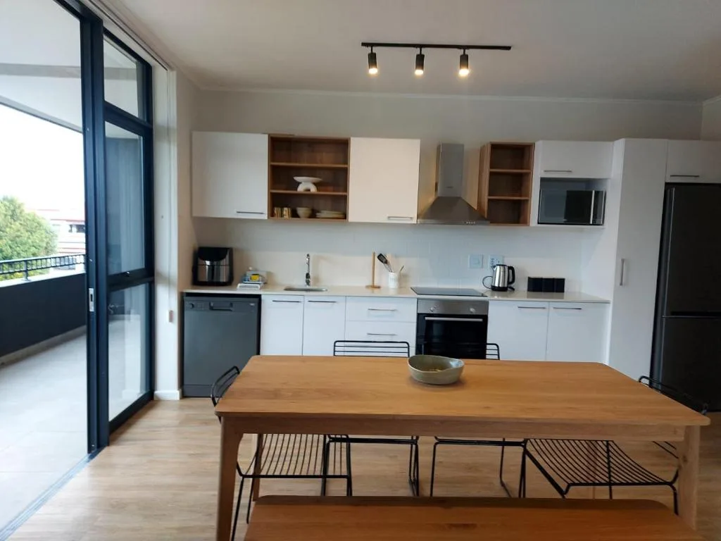 Modern kitchen with white cabinetry, wooden dining table, and stainless steel appliances