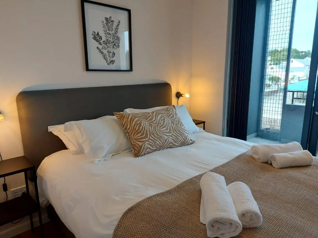 Contemporary bedroom with dark headboard, white linens, rolled towels, and garden view