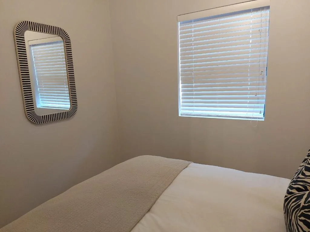 Bright bedroom with double bed, decorative mirror, and modern window blinds