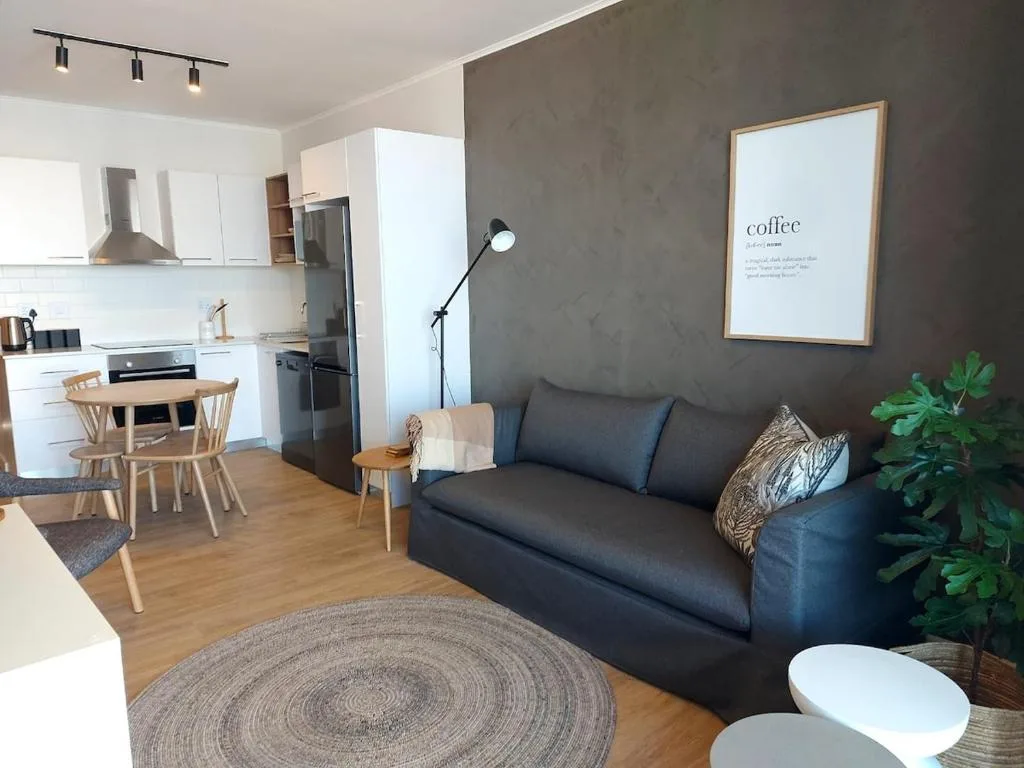 Modern lounge with dark sofa, round rug, and open-plan kitchen view