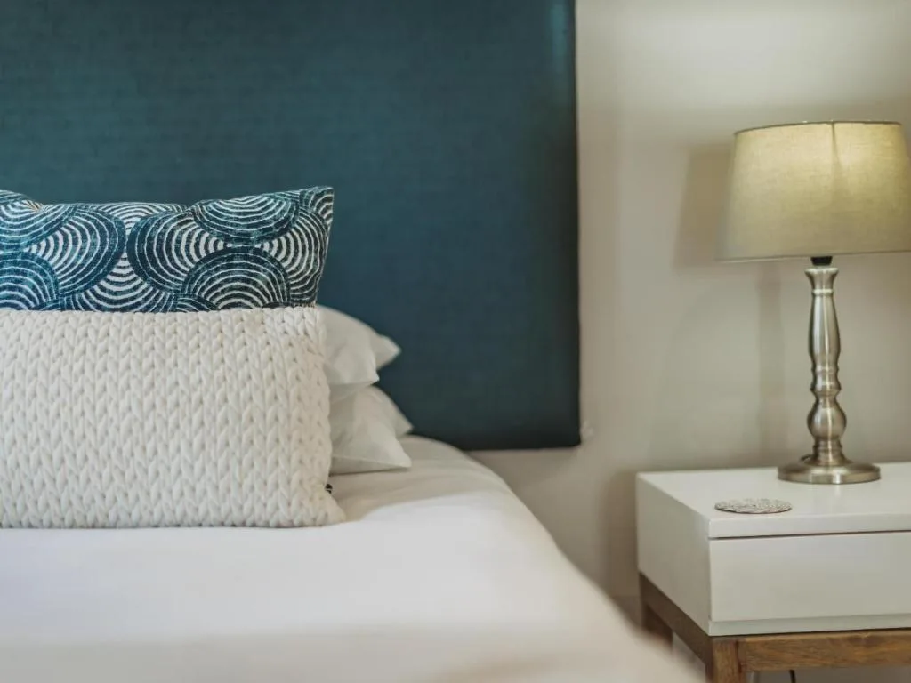Modern bedroom with teal accent wall, white pillows, and bedside lamp