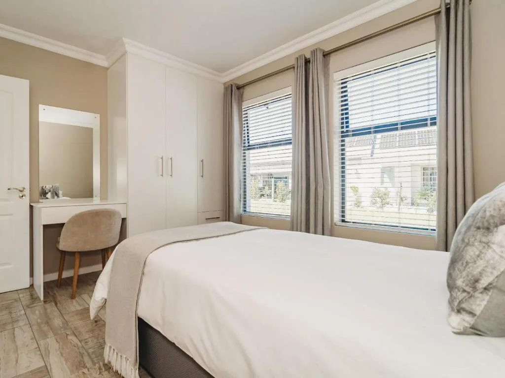 Bright bedroom with queen bed, vanity desk, and large windows overlooking gardens