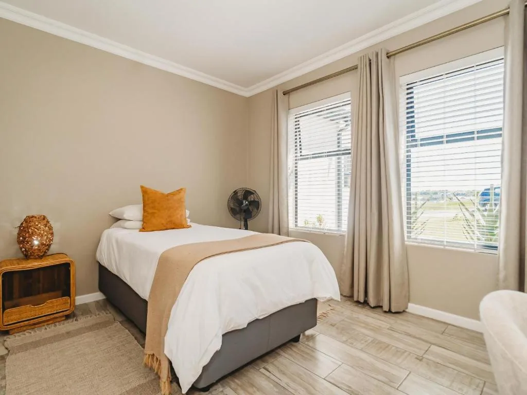 Bright bedroom with single bed, orange accent pillow, and expansive windows overlooking landscape