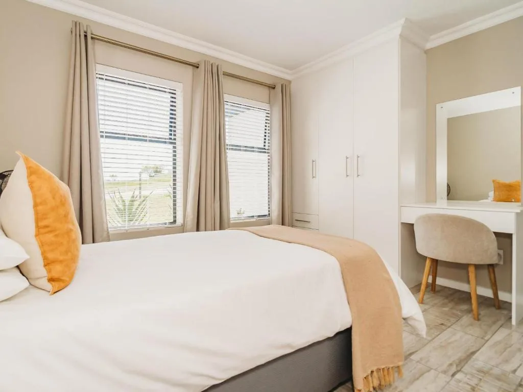 Bright bedroom with queen bed, vanity desk, and large windows overlooking garden