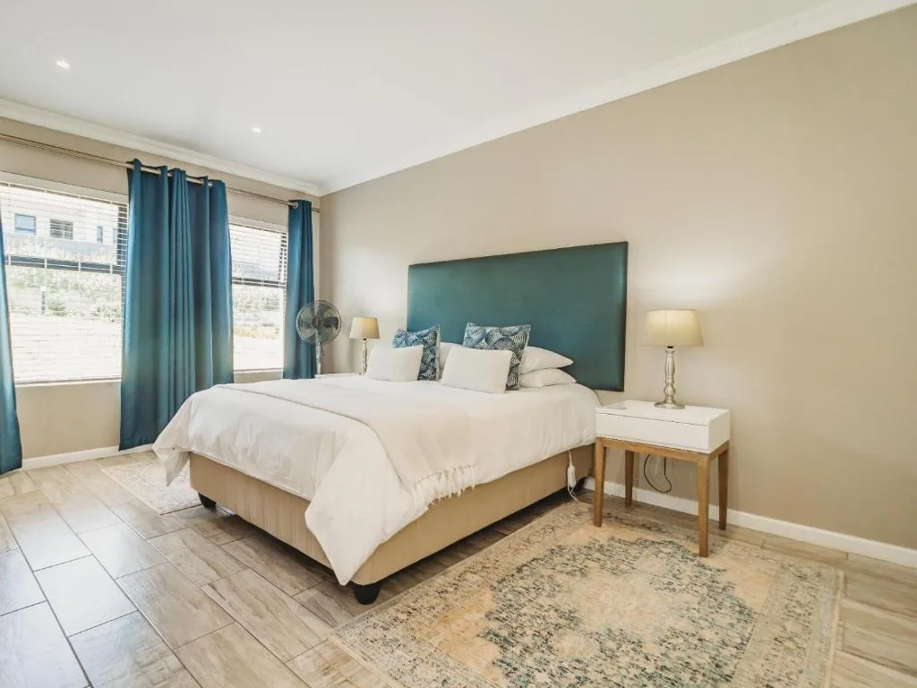Spacious bedroom with green headboard, white bedding, teal curtains, and side tables