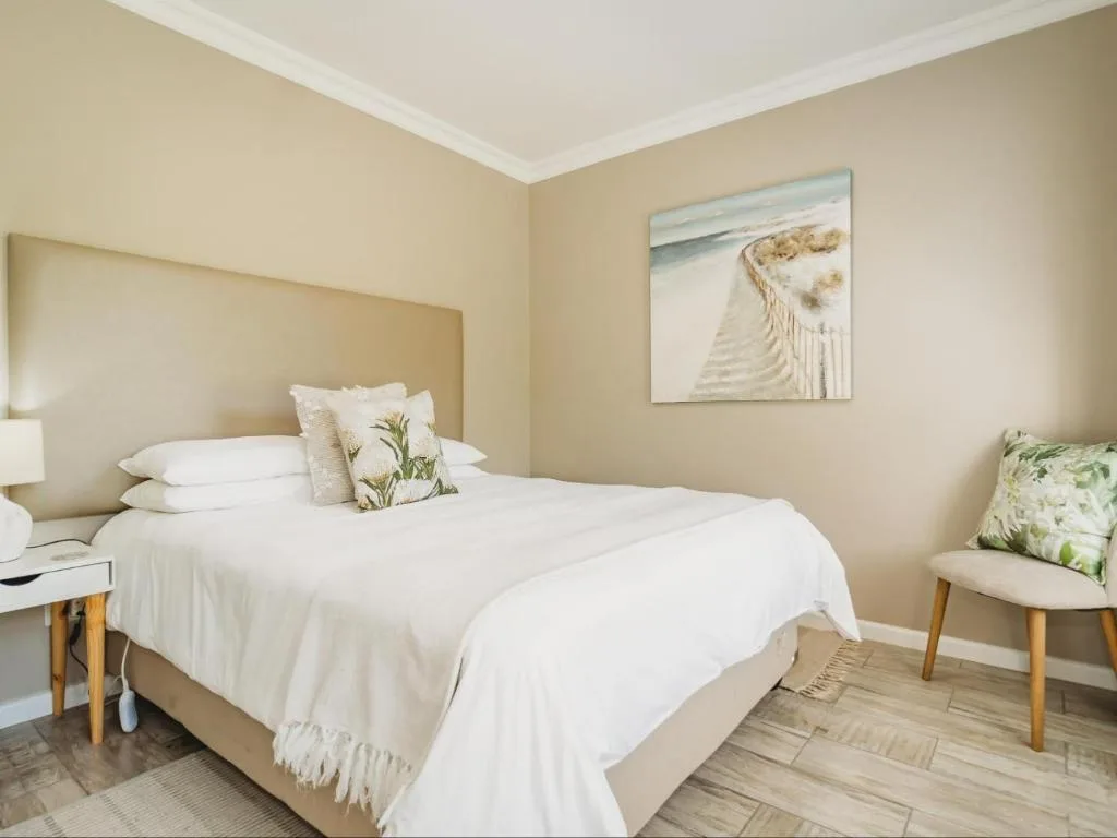 Spacious bedroom with white bedding, coastal artwork, and natural light
