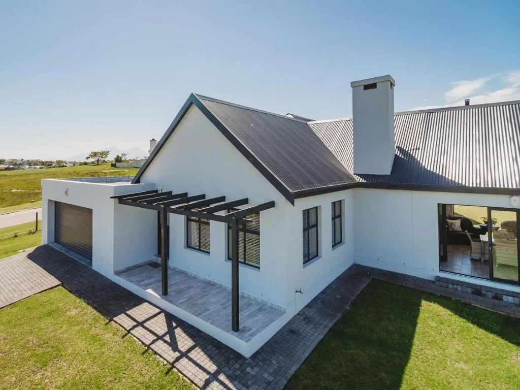 Modern white farmhouse with black pergola and manicured garden grounds