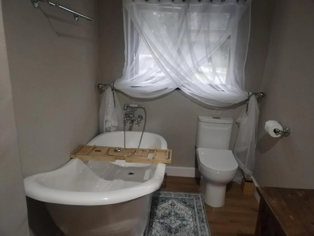 Bathroom with curved bathtub, toilet, and sheer white window curtains