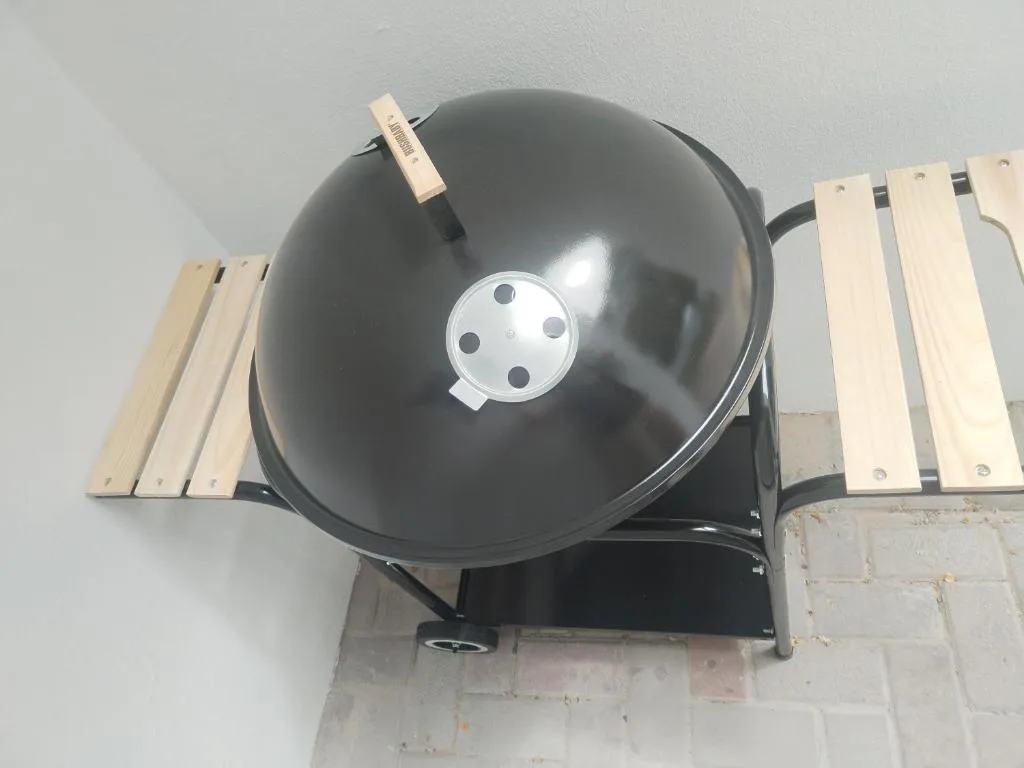 Black globe braai grill with wooden armrests on brick surface