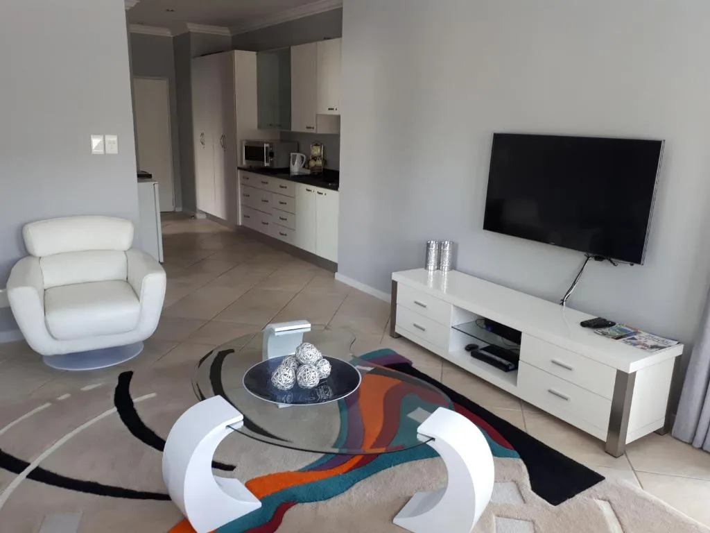 Modern living room with white armchair, TV unit, and open-plan kitchen access