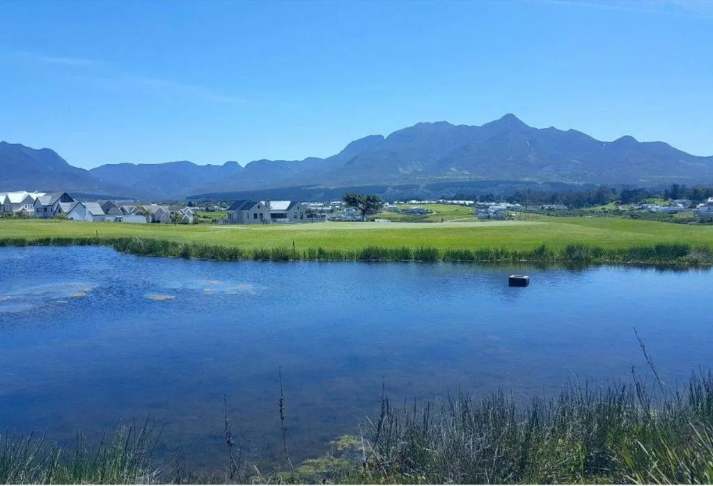 Lagoon view with mountains, green fields, and residential properties in distance