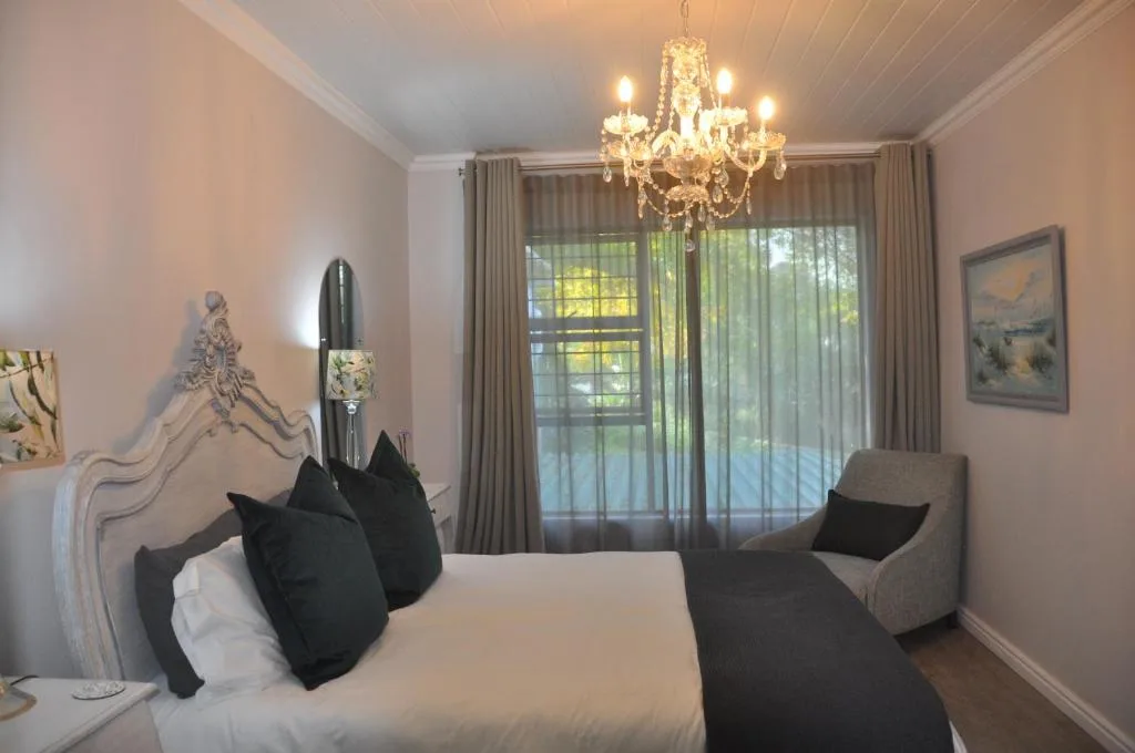 Elegant bedroom with white bed, black pillows, crystal chandelier, garden views