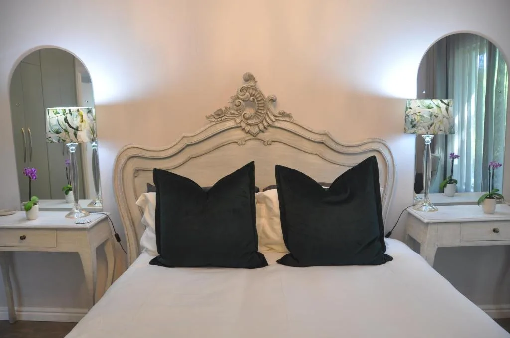 Elegant bedroom with ornate headboard, black pillows, twin vanities with mirrors