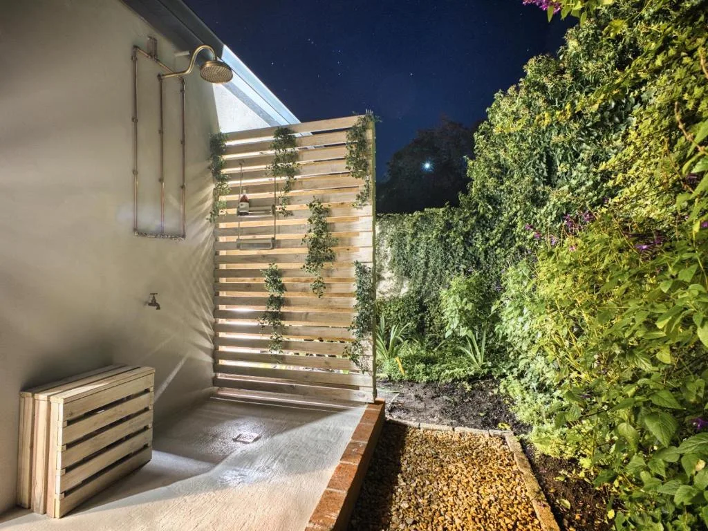 Outdoor shower area with wooden privacy screen and lush green plant walls