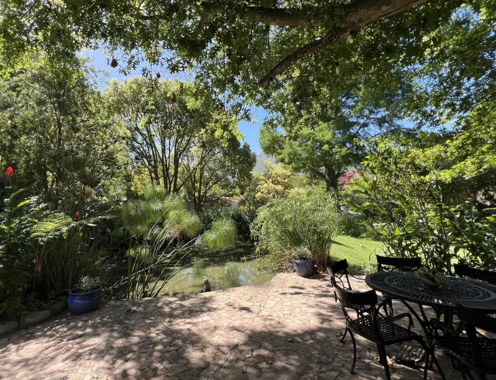Shaded garden patio with seating, pond, and mature trees