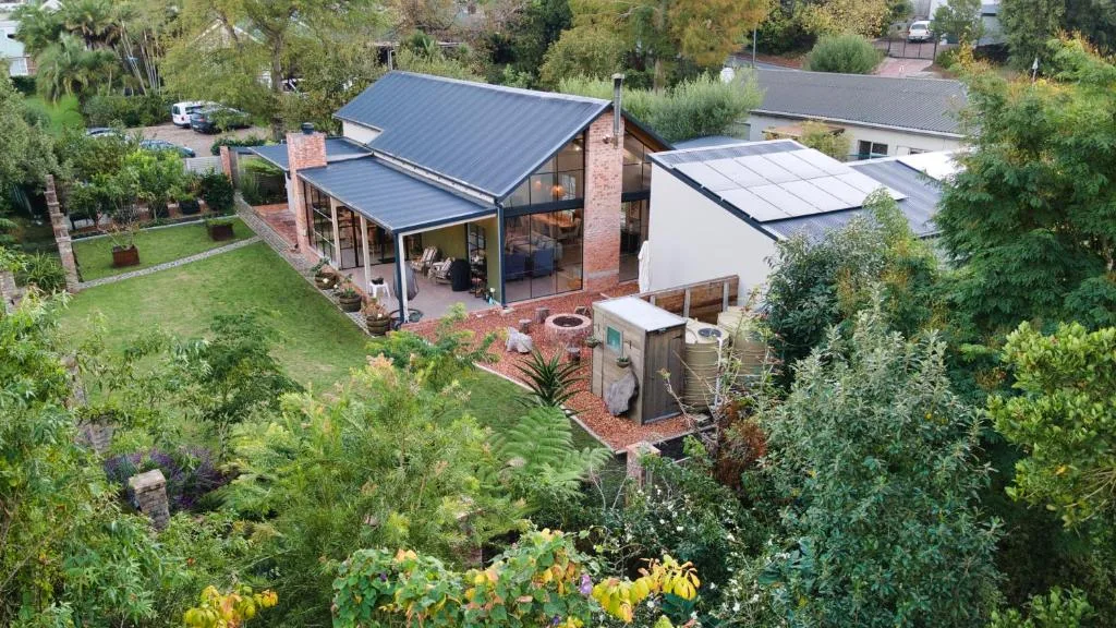 Modern brick home with dark roof and large windows surrounded by lush garden