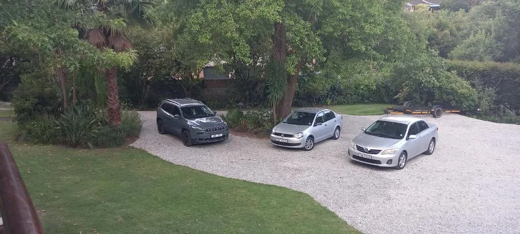 Gravel driveway with three parked cars surrounded by lush garden and trees