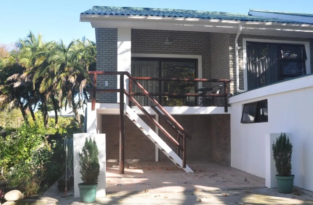 Modern home entrance with brick facade, wooden railing stairs, and tropical landscaping.