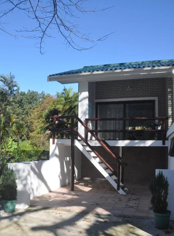Modern apartment entrance with wooden deck and metal railings, lush garden surroundings