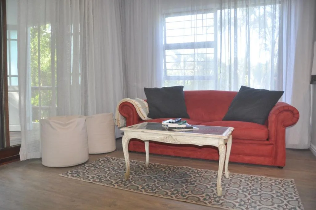 Bright lounge with red sofa, cream coffee table, and garden views through large windows
