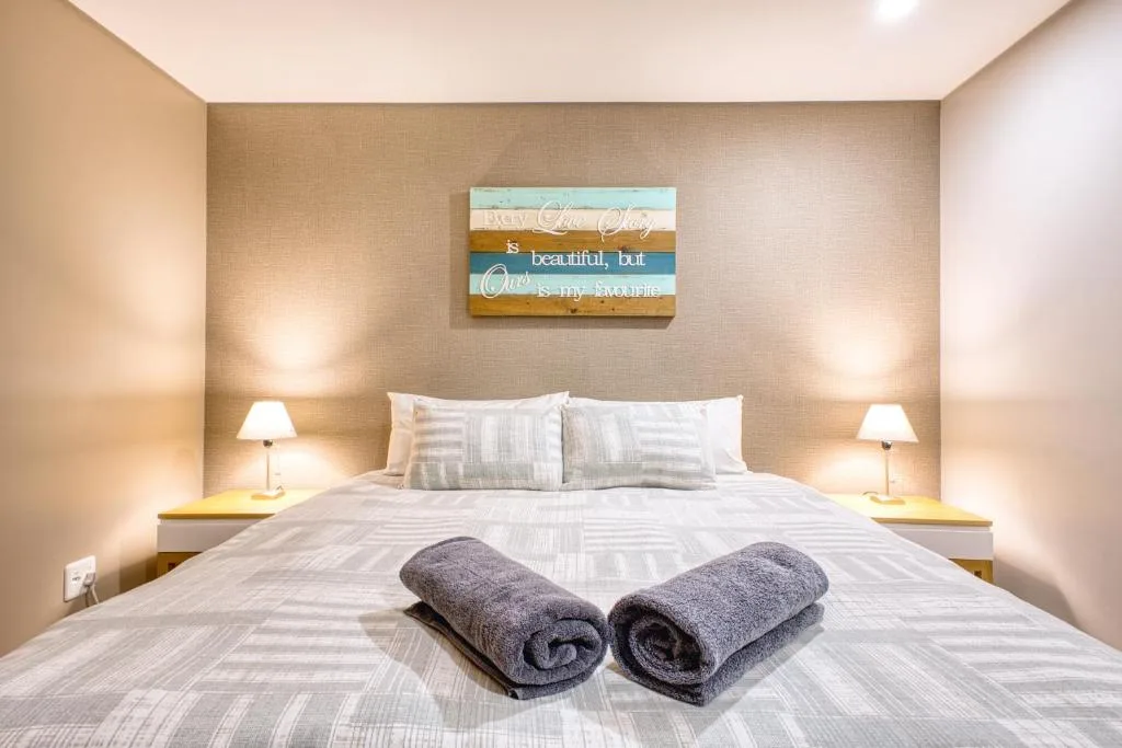 Modern bedroom with queen bed, rolled towels, and inspirational wall art