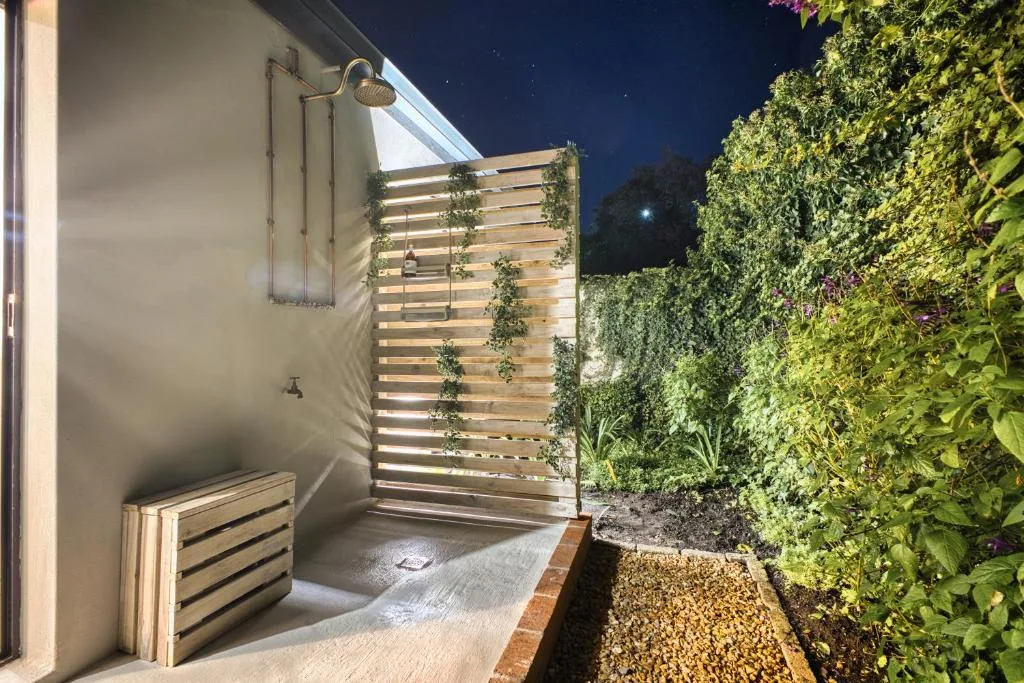 Outdoor shower area with wooden screen and lush green climbing plants at night