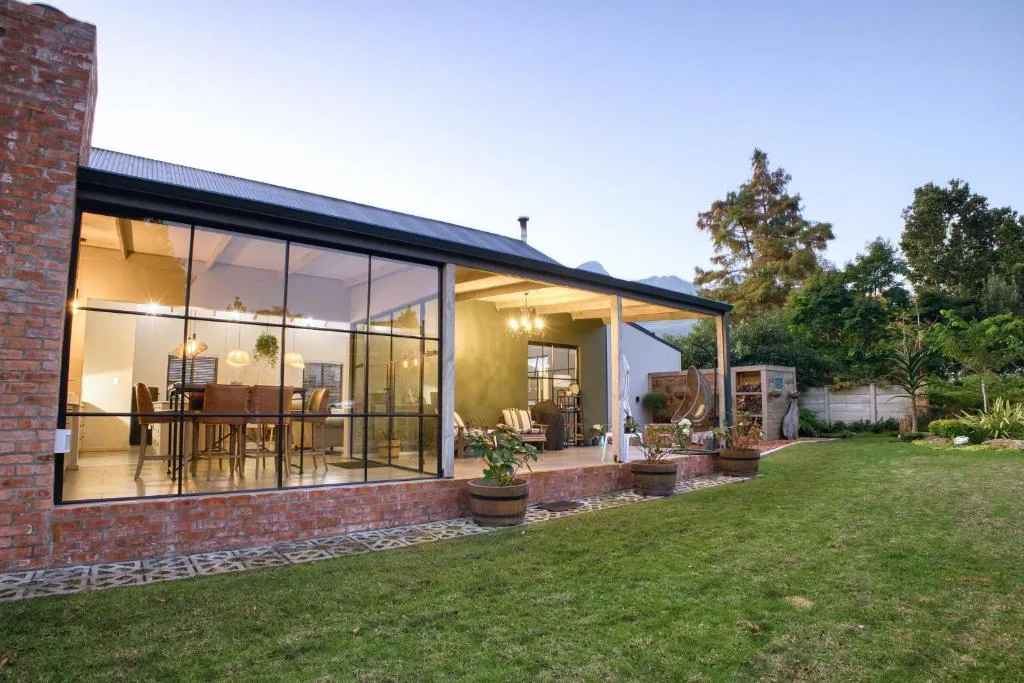 Modern brick villa with large glass doors opening onto manicured garden lawn
