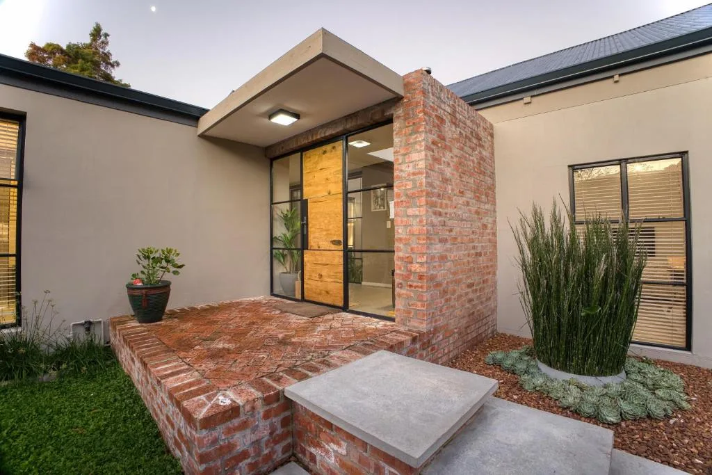 Modern villa entrance with brick chimney, wooden door, and manicured garden courtyard
