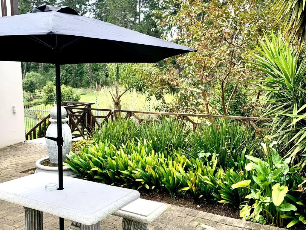 Shaded patio with black umbrella overlooking lush garden landscape